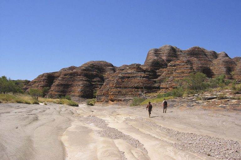 Twee wandelaars in de droge bedding van Piccaninny Creek in Purnululu National Park, West-Australië, met de gestreepte Bungle Bungle-koepelrotsen op de achtergrond