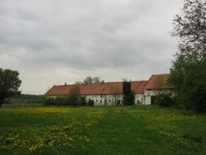 Grote oude boerderij met rode daken in Biskupice, Tsjechië, omgeven door hoge bomen onder een bewolkte lucht