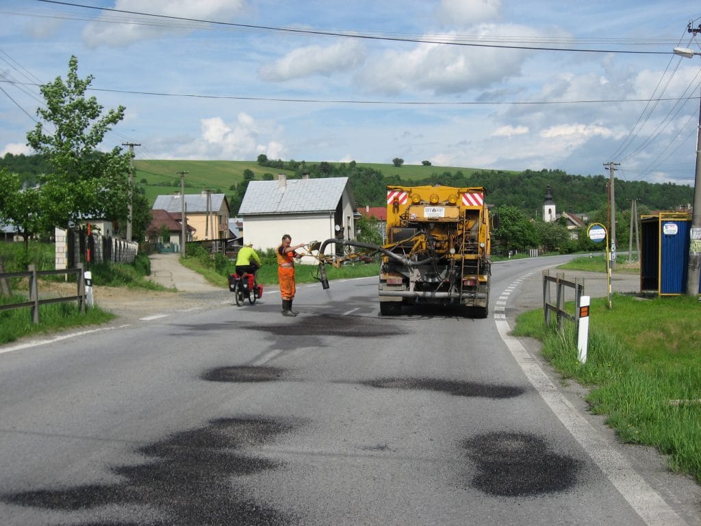 Geel wegenbouwmachien en werkers in oranje hesjes herstellen vorstschade aan de weg bij Gerlachov, Slowakije
