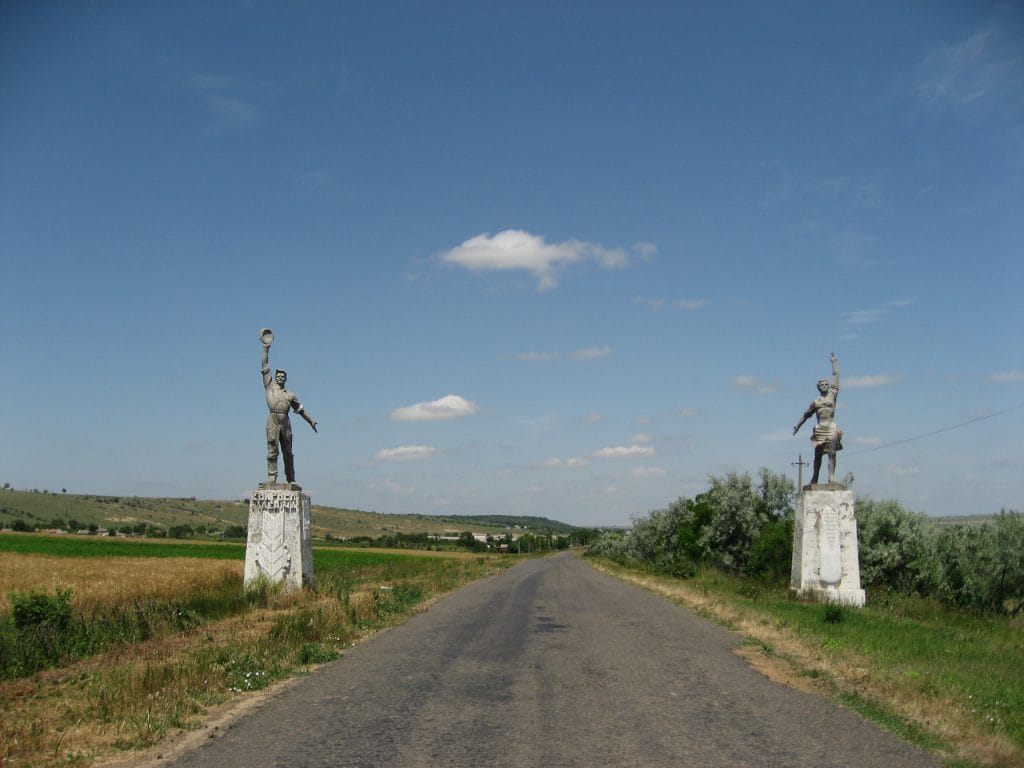 Twee Sovjet-era standbeelden van een arbeider en een vrouw op sokkels langs de weg in Oekraïne, onder een blauwe lucht met wolken