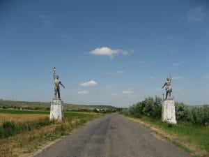 Twee Sovjet-era standbeelden van een arbeider en een vrouw op sokkels langs de weg in Oekraïne, onder een blauwe lucht met wolken