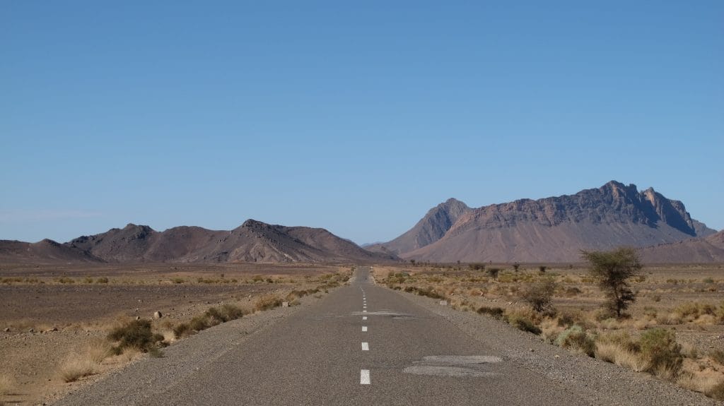 Rechte verlaten weg door kaal Marokkaans woestijnlandschap met rotsige bergen op de achtergrond