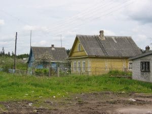 Rij houten huizen met verweerde golfplaten daken langs een modderige weg in Rusland, elektriciteitsleidingen boven de straat