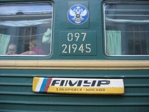 Zijkant van Russische treinwagon met dubbelkoppige adelaar en wagonnummer 21945, vrouw kijkt door raam
