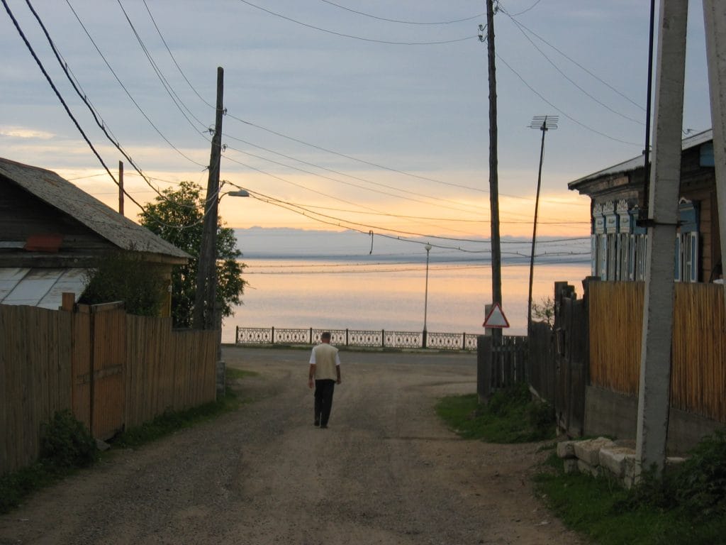 Smal straatje in Listvyanka met houten hekken en elektriciteitspalen en zicht op het Baikalmeer bij zonsondergang