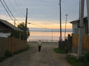 Smal straatje in Listvyanka met houten hekken en elektriciteitspalen en zicht op het Baikalmeer bij zonsondergang