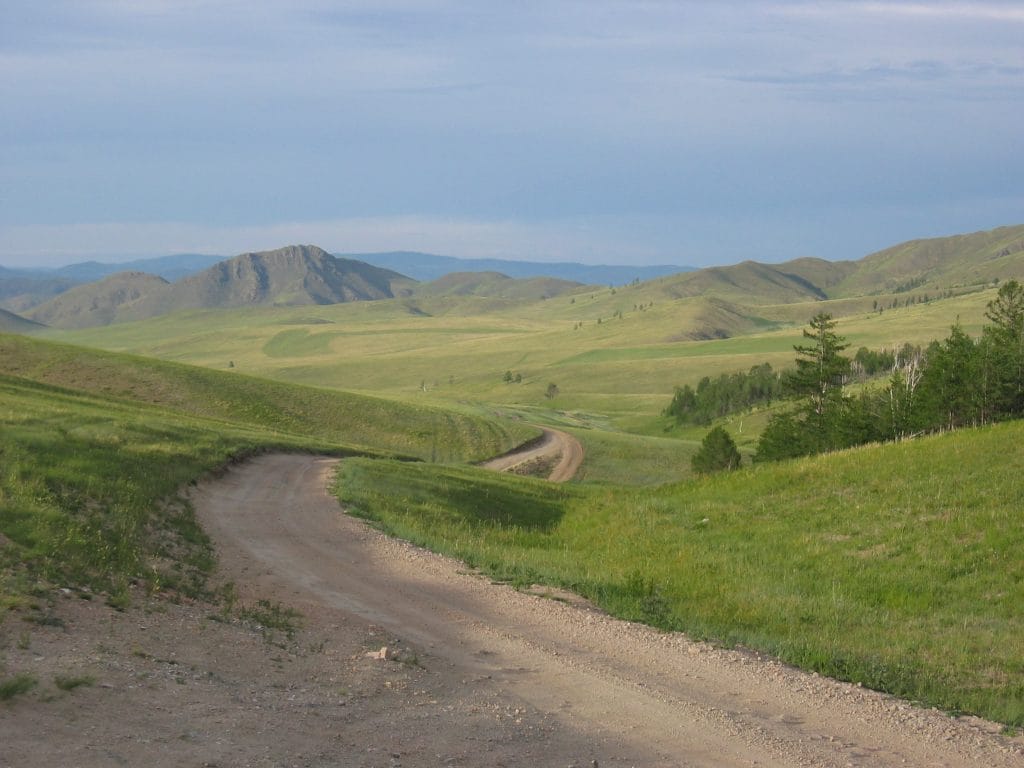 Breed Mongools steppenlandschap met groene heuvels en een lege onverharde weg richting Amarbayasgalant Khiid