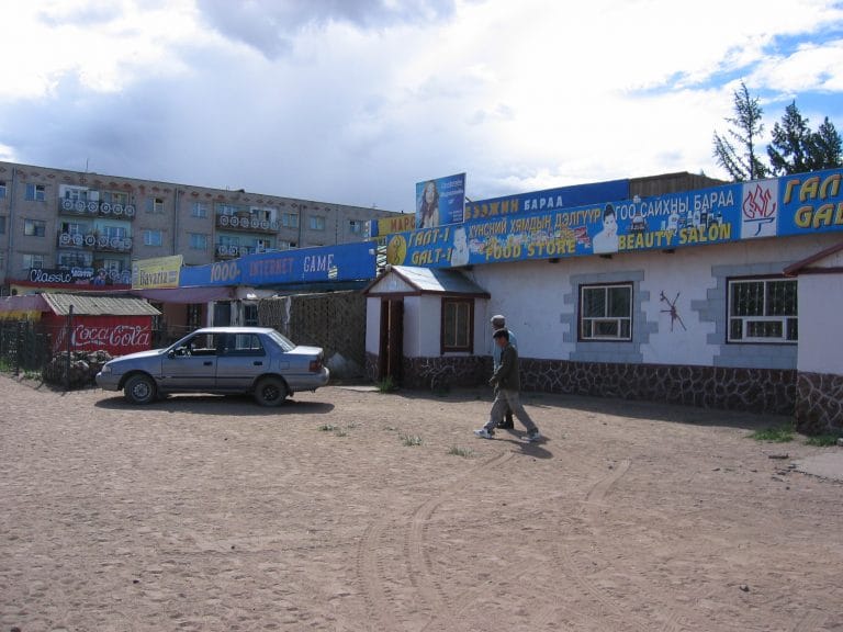 Winkelcentrum in Murun, Mongolië, met felle blauwe gevel, Cyrillisch schrift en borden als Food Store en Beauty Salon