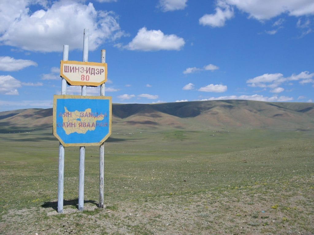 Mongools verkeersbord in Cyrillisch schrift met Шинэ-Идэр 80 bij de provinciegrens van Zavkhan, met blauwe lucht en steppe op de achtergrond