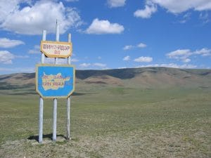 Mongools verkeersbord in Cyrillisch schrift met Шинэ-Идэр 80 bij de provinciegrens van Zavkhan, met blauwe lucht en steppe op de achtergrond