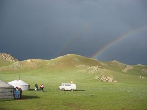 Dubbele regenboog boven een tentenkamp in de steppe bij Terkhiin Tsagaan Nuur in Mongolië, onder een donker wolkendek