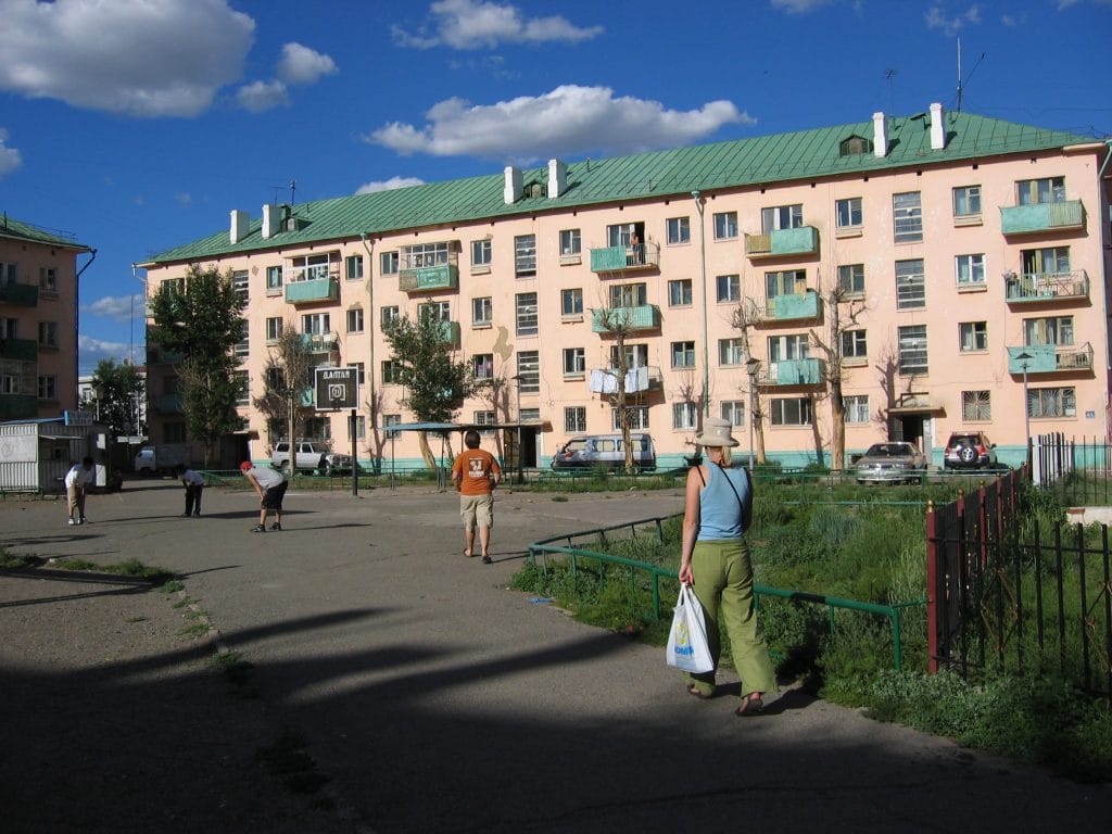 Roze Sovjet-era flatgebouw met groene daken en kleine balkons in Ulaanbaatar, Mongolië, met een basketbalring op de voorgrond