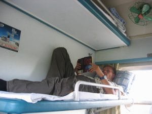 Bovenste bunk in de harde sleeperklasse van een Chinese trein, met groene ventilator en Chinese poster