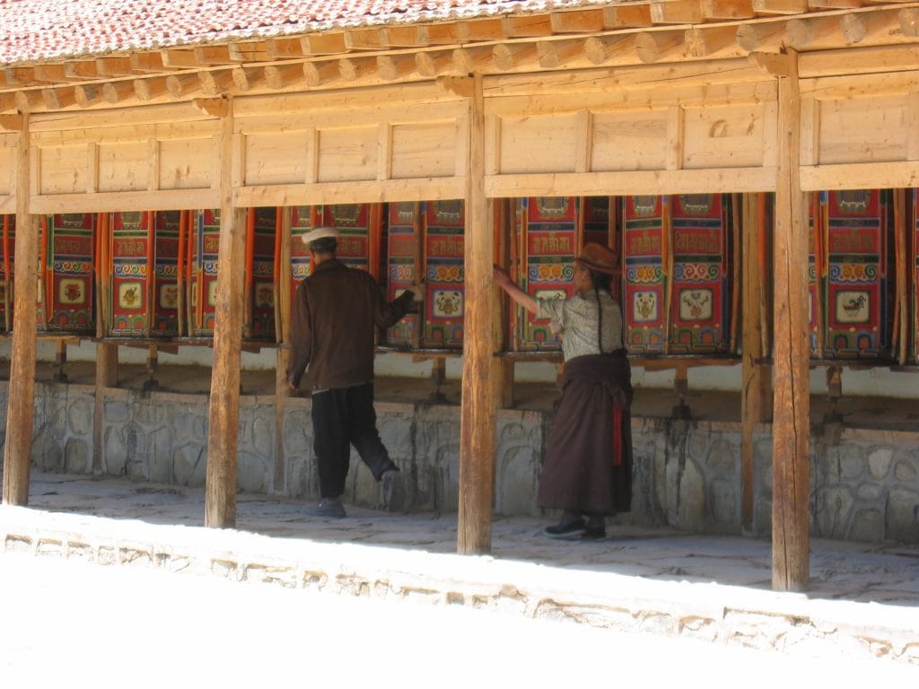 Twee bezoekers bij de geschilderde gebedsrollen langs de houten galerij van het Labrang-klooster in Xiahe
