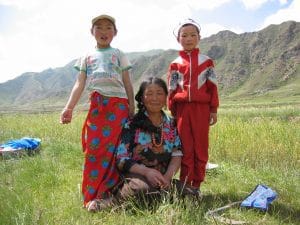 Tibetaanse moeder en twee kinderen in kleurrijke kleding poseren voor groene berghellingen bij Xiahe