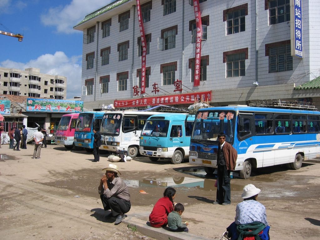 Busstation van Hezuo met rijen blauwe bussen voor een gebouw met rode banners en Chinese karakters