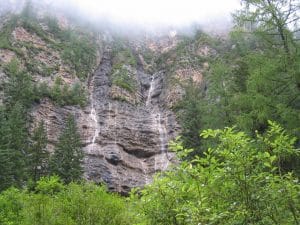 Steile rotsige kliffen met mist, een dunne waterval en naaldbomen in de vallei van Jiuzhaigou