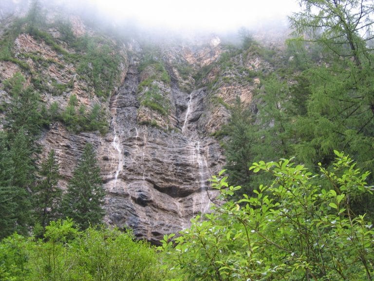 Steile rotsige kliffen met mist, een dunne waterval en naaldbomen in de vallei van Jiuzhaigou