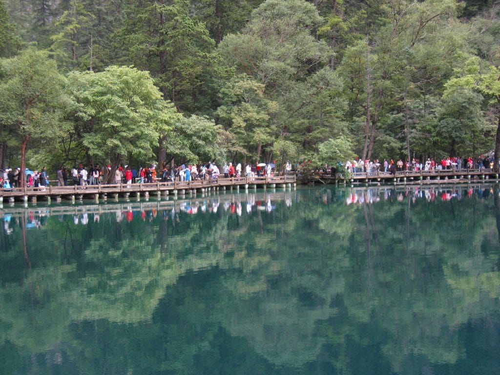 Honderden toeristen op een houten boardwalk langs een turquoise meer omgeven door dichte bossen in Jiuzhaigou