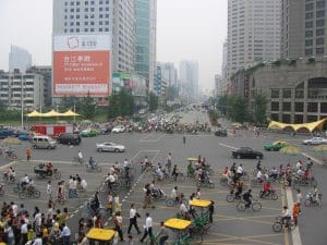 Drukke kruising in Chengdu gezien van boven met honderden fietsers, scooters en riksja's en een verkeersagent in het midden