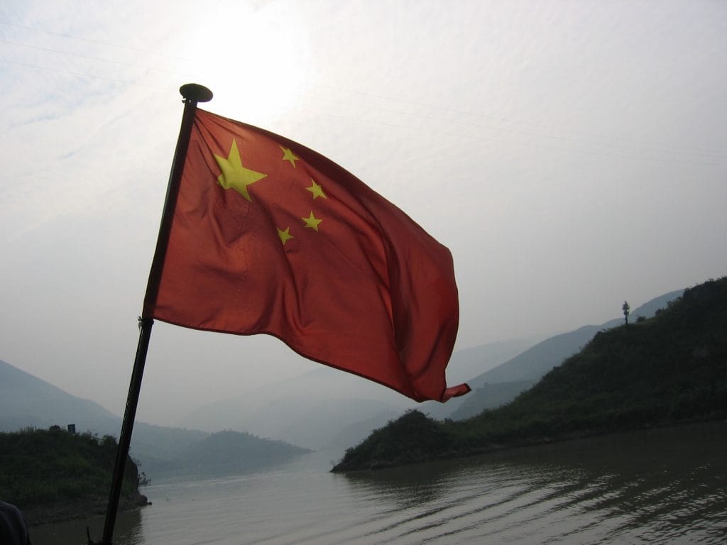 Rode Chinese nationale vlag met vijf gele sterren wapperend in de wind tegen een bleke hemel