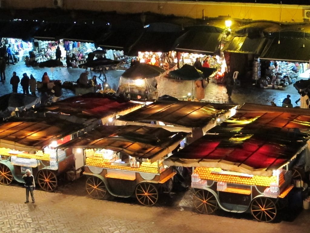 Drukke avondmarkt op de Djemaa el-Fna in Marrakesh met verlichte kraampjes en versgeperste jus d'orange