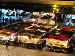 Drukke avondmarkt op de Djemaa el-Fna in Marrakesh met verlichte kraampjes en versgeperste jus d'orange