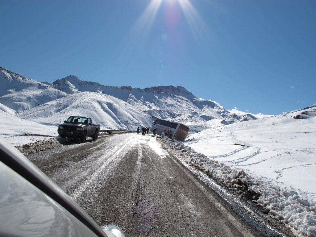 Auto op een besneeuwde bergpas in de Hoge Atlas van Marokko met felle zon en sneeuwbedekte hellingen