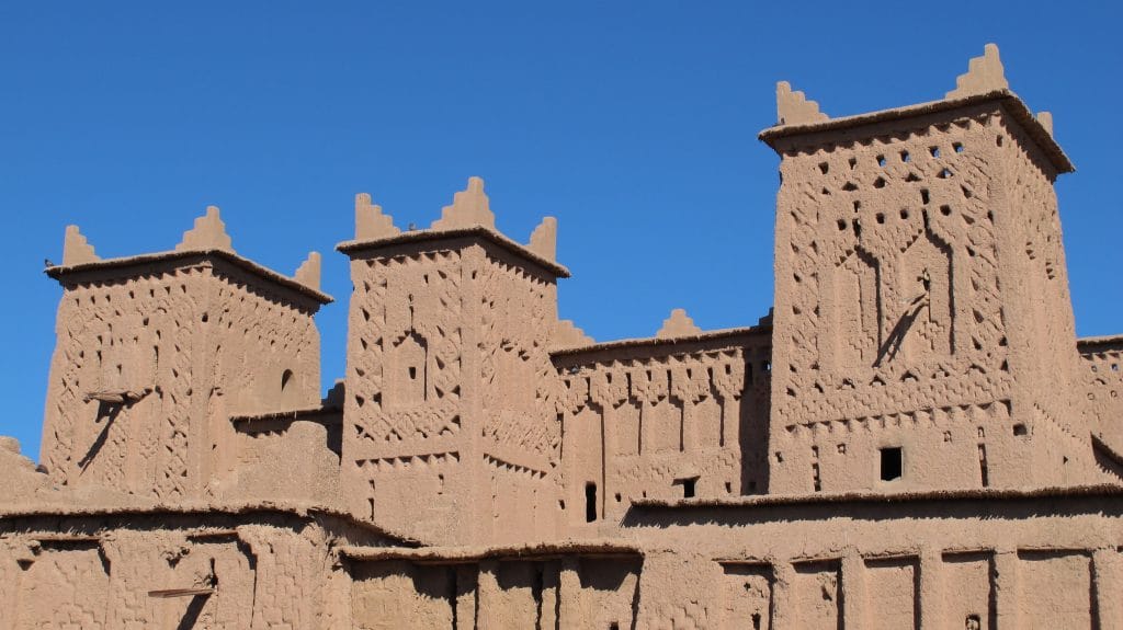 Drie hoge torens van een Marokkaanse kasbah gebouwd van leem en stro met geometrische versieringen tegen een strakblauwe lucht