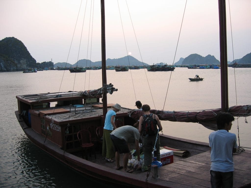 Uitzicht vanaf een boot op de karst-eilanden en jonks in Hạ Long Bay, Vietnam, bij schemering met een visser in een roeiboot
