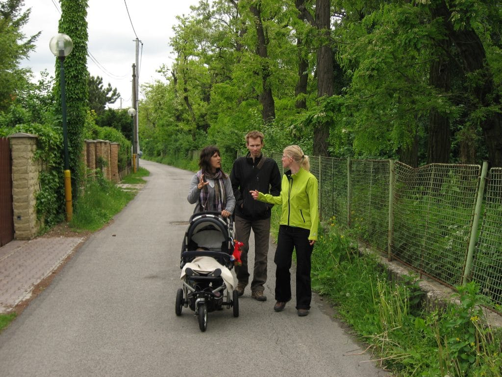 Drie mensen wandelen op een groen boomrijk pad in een woonwijk van Bratislava, Slowakije