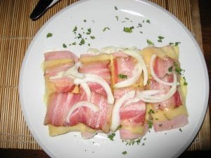 Wit bord met brinza, ham, uienringen en verse peterselie op een bamboe placemat in Terchová, Slowakije