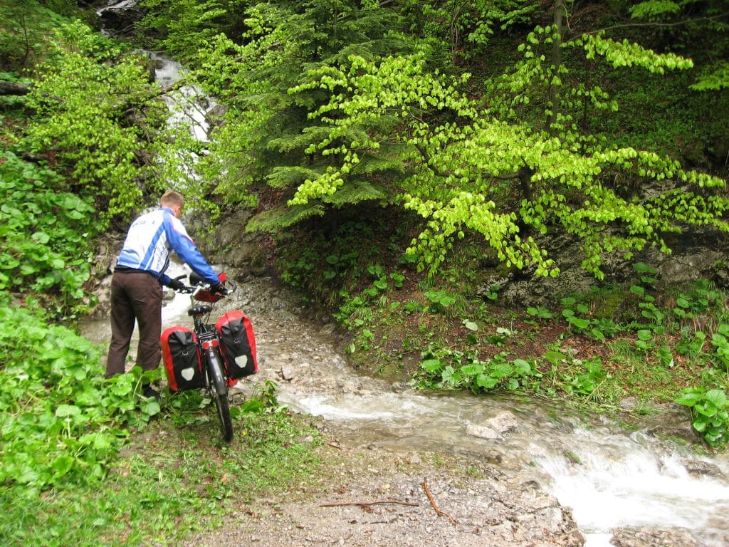Fietser in blauw die zijn fiets over een rotsig pad leidt langs een waterval in de Kvačianska dolina, Slowakije