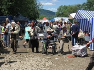 Drukke buitenmarkt in Staryi Kosiv, Oekraïne, met lokale bewoners in traditionele kledij en blauwe markttenten, groene Karpatische heuvels op de achtergrond