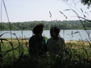 Twee mensen in silhouet kijken uit over een meertje bij Bershad in Oekraïne, met de dorpskerk en groene bomen aan de overkant