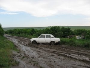 Modderige onverharde weg in Sukha Zhurivka, Oekraïne, na een hoosbui veranderd in zware klei, met groene heuvels op de achtergrond