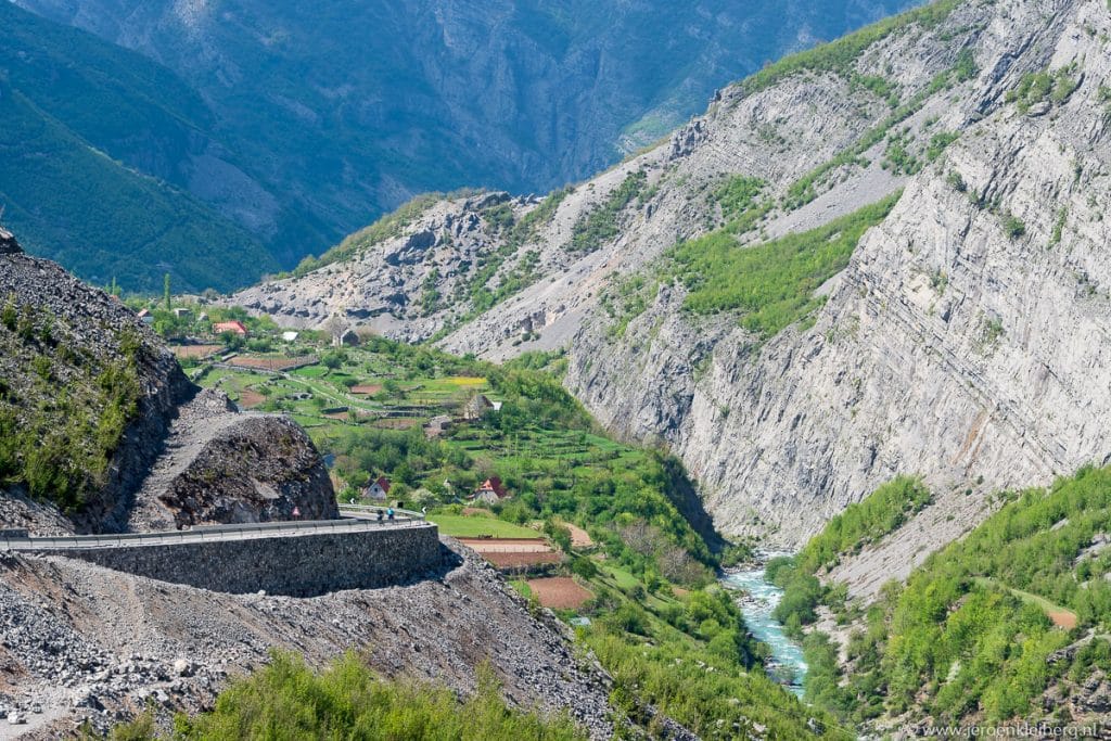 Steile bergweg daalt af door een diepe rotsachtige kloof in Albanië, met turquoise rivier en groene vegetatie op de bodem van de vallei