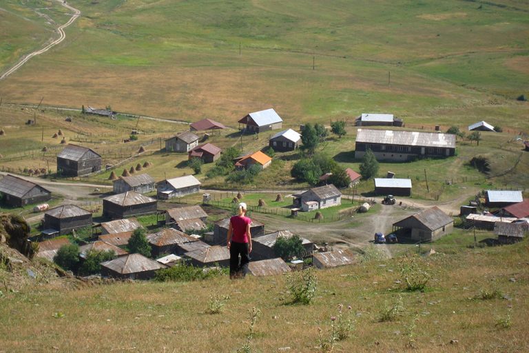 Vrouw daalt af naar het bergdorp Omalo in de Tusheti-regio van Georgië, met traditionele houten huizen en hooibergen op de achtergrond