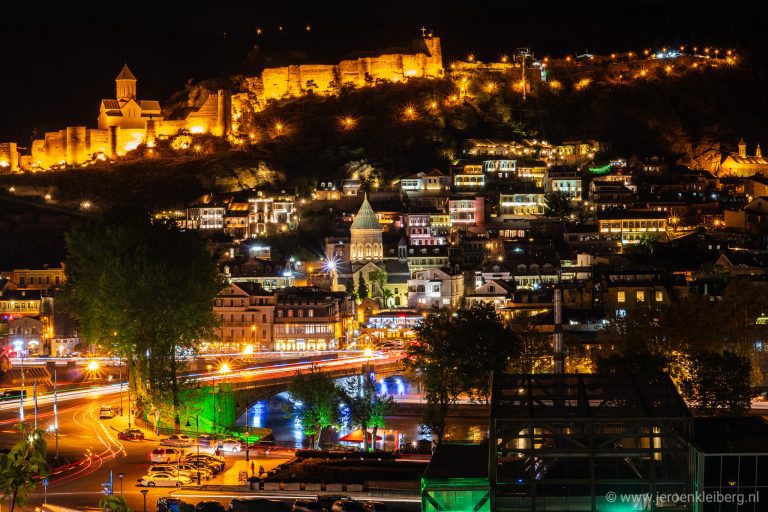 Nachtfoto van de verlichte oude stad van Tbilisi in Georgië, met het Narikala-kasteel op de heuvel en kleurrijke traditionele huizen op de voorgrond