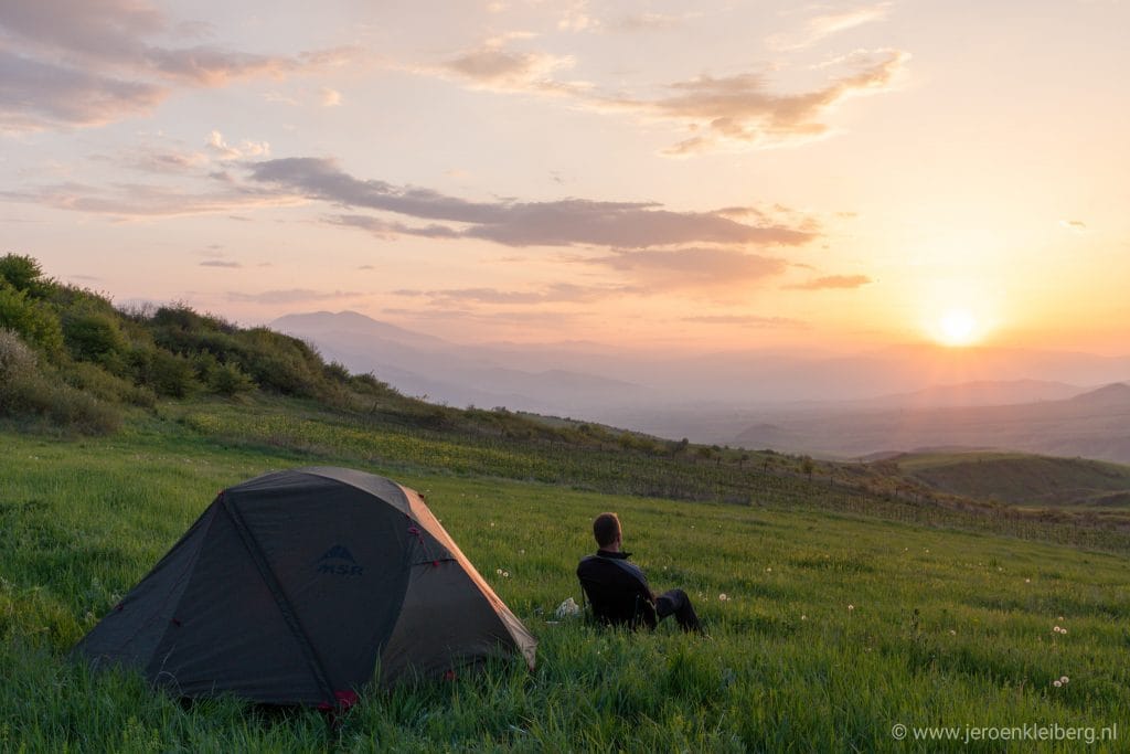 Zonsondergang boven de groene heuvels van Armenië met oranje en roze wolken aan de horizon, gezien vanaf een kampeerlocatie