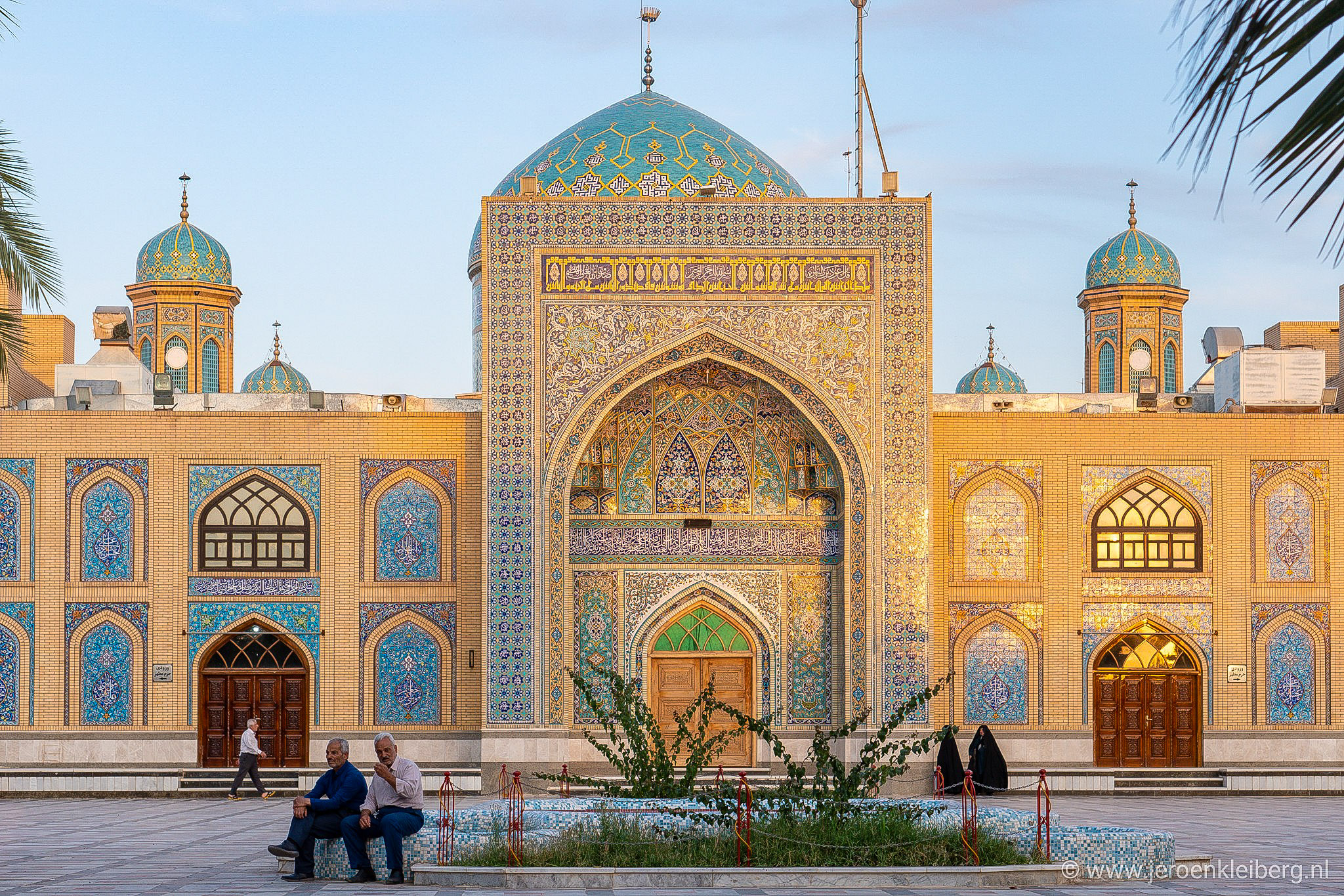 Twee mannen zitten voor de betegelde moskee van Tabas in Iran in het avondlicht