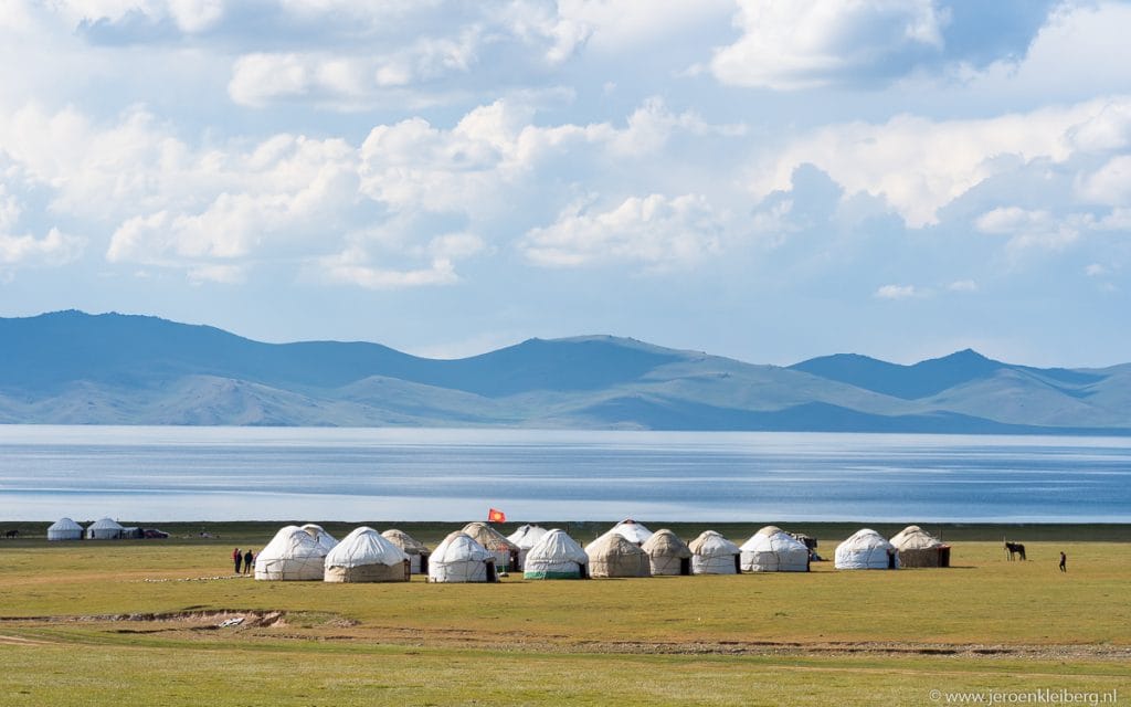 Rij witte yurts op de groene oever van het Issyk-Kulmeer in Kirgizistan met blauwe bergketen en bewolkte lucht op de achtergrond