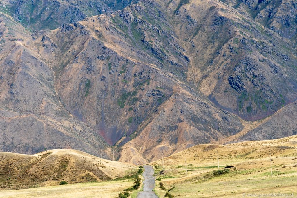 Smalle asfaltweg die verdwijnt in een verlaten rotsachtige bergkloof in Kazachstan met bruine en grijze bergwanden