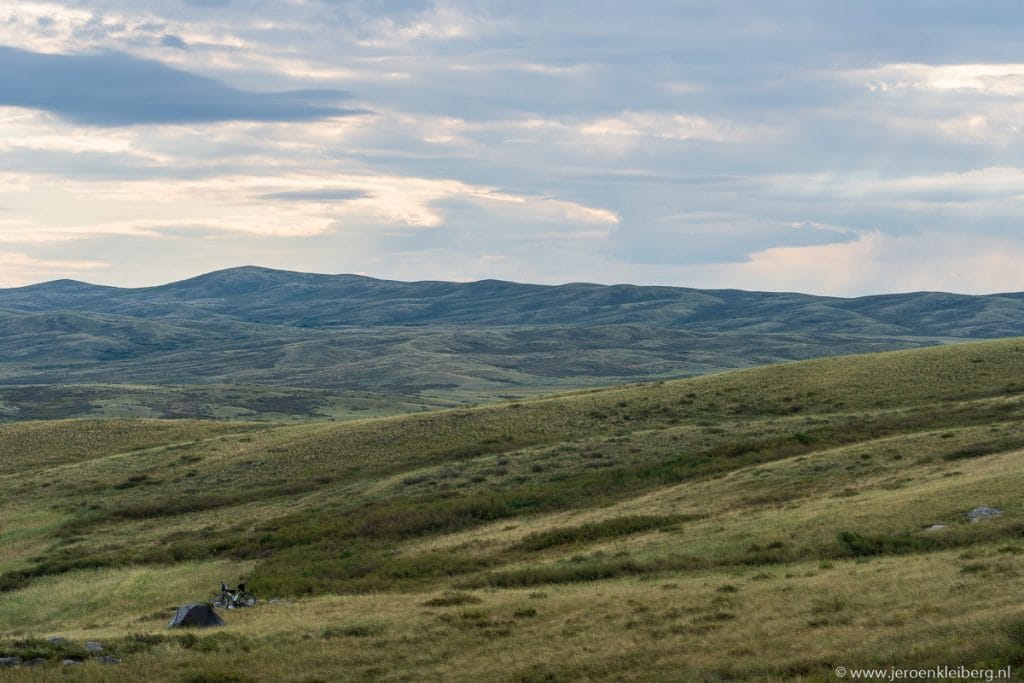 Kleine tent nauwelijks zichtbaar in de uitgestrekte groene glooiende heuvels van Kazachstan onder een bewolkte lucht
