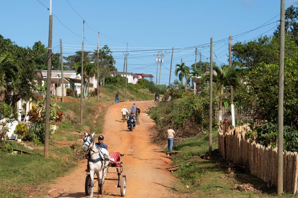 Verkeer op een rode onverharde weg door het heuvelachtige landschap van Cuba met palmbomen