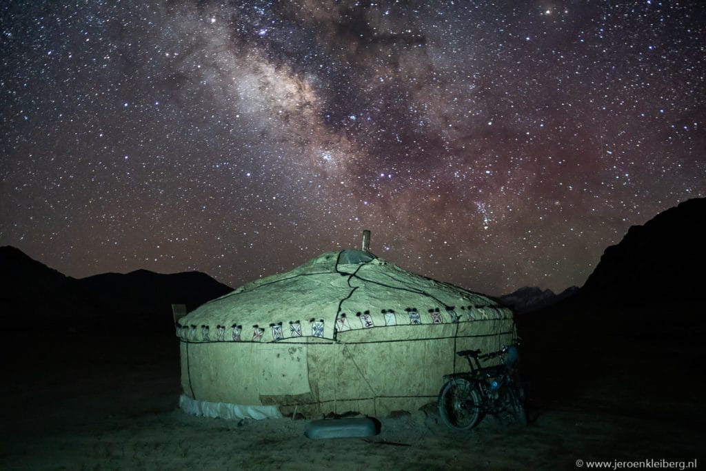 Verlichte yurt met een fiets ertegenaan op de Pamir hoogvlakte in Tadzjikistan, met de Melkweg in de nachtelijke hemel