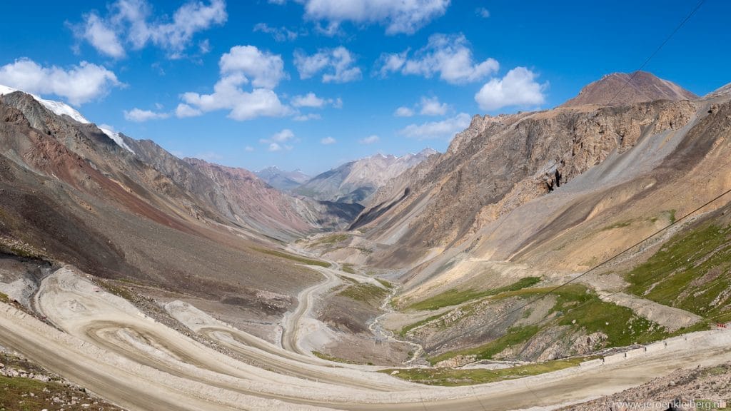 Panoramische foto van een kronkelende bergweg door een kale rotsachtige bergpas in Kirgizistan, blauwe lucht met wolken