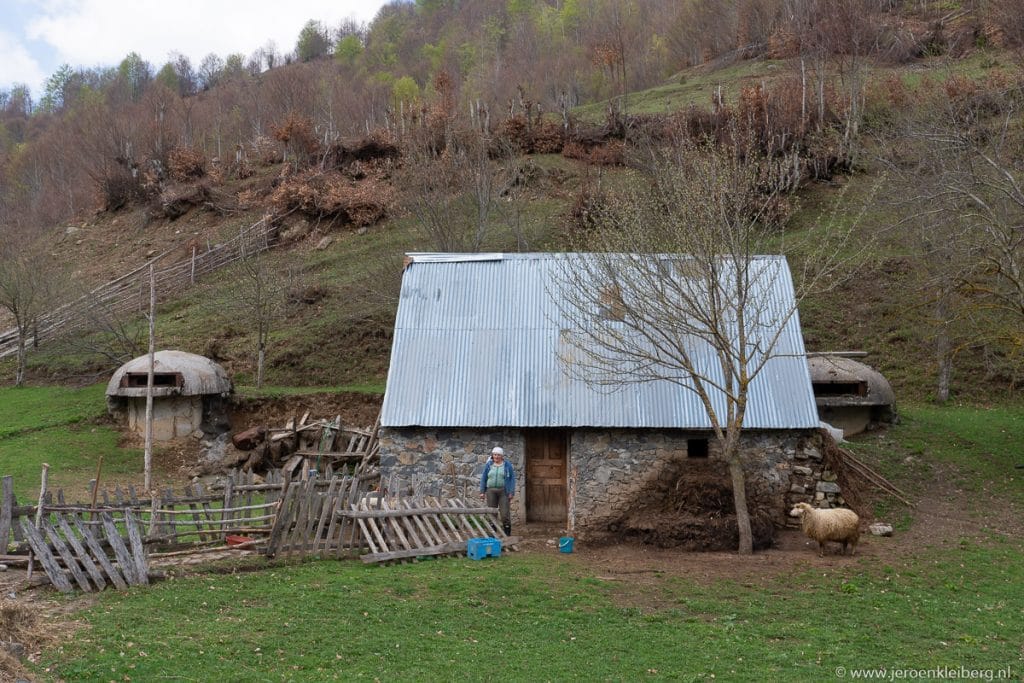 Traditionele stenen boerderij met golfplaten dak in de Albanese bergen, met een schaap in de tuin en betonnen bunkers uit het communistische tijdperk