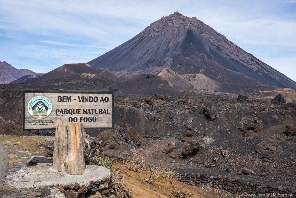 Welkomstbord van het Parque Natural do Fogo in Kaapverdië met de Pico do Fogo-vulkaan en zwart lavalandschap op de achtergrond
