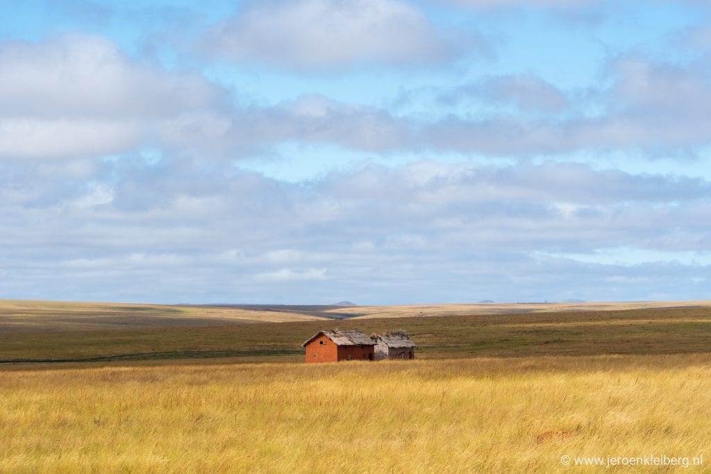 Eenzame rode boerderij met rieten dak op het kale hoogplateau van Madagaskar onder een uitgestrekte blauwe hemel met wolken